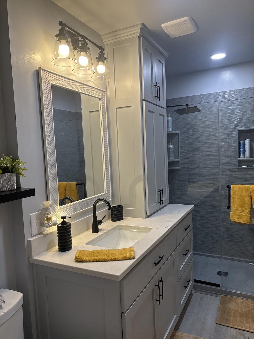 A finished bathroom with a grey vanity, quartz top, black fixtures and a tiled walk-in shower